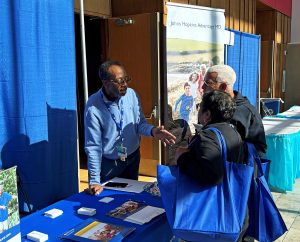 Johns Hopkins Advantage MD employee stands behind table and provides educational material about our Medicare plans while some visitors read the material.