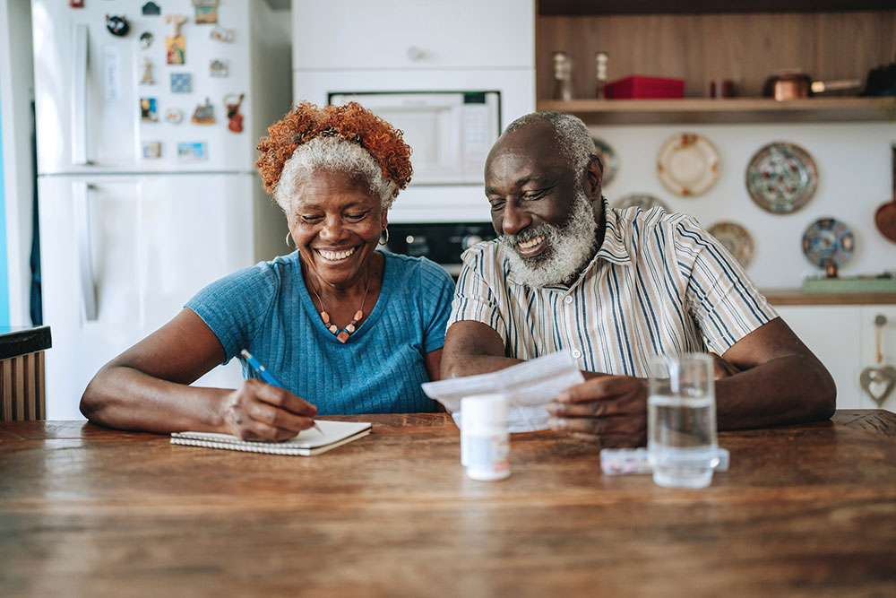 mature African-American couple sitting at their kitchen table looking at a piece of paper and taking notes in a notepad
