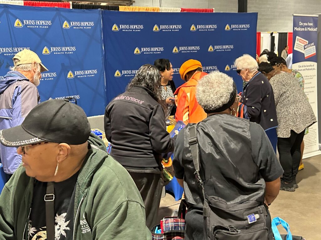 People interacting at a Johns Hopkins Advantage MD information booth during an event.