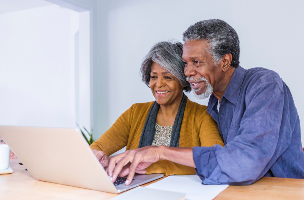 An African-American couple using a laptop, smiling. Wearing casual clothes.