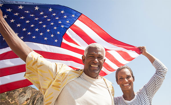 Mature African American couple standing outdoors holding an American flag