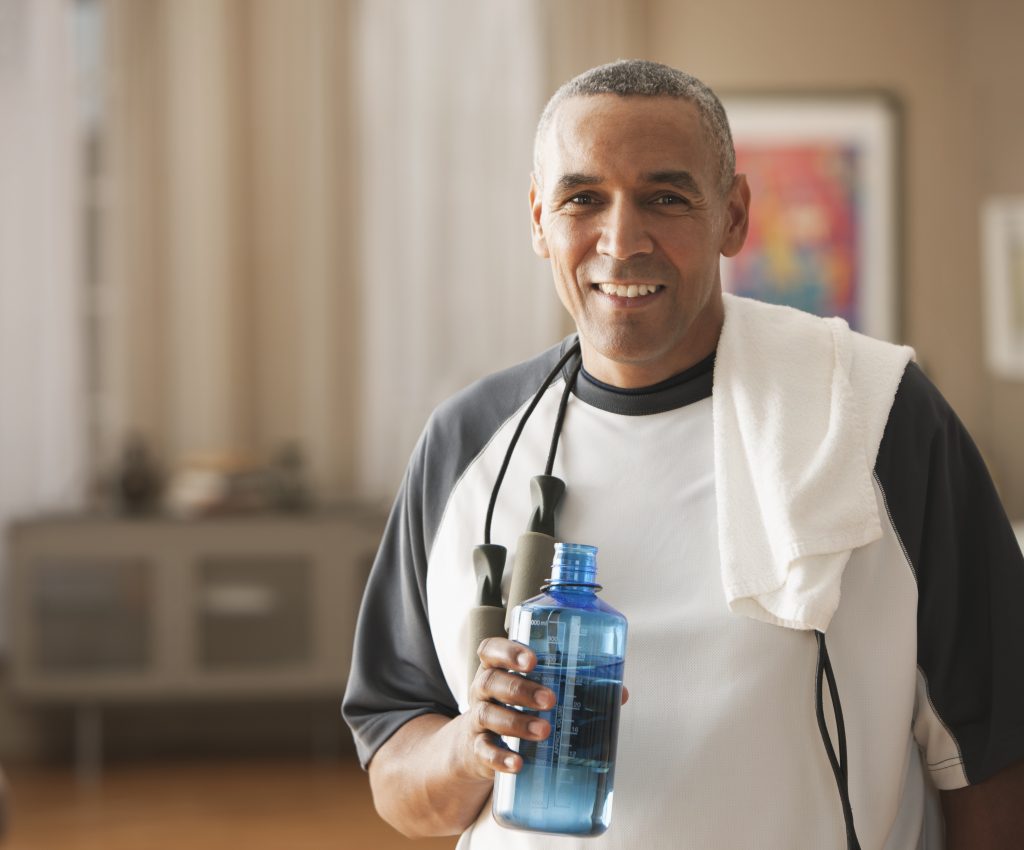 senior man wearing sport outfit, holding bottle of water indoors. 