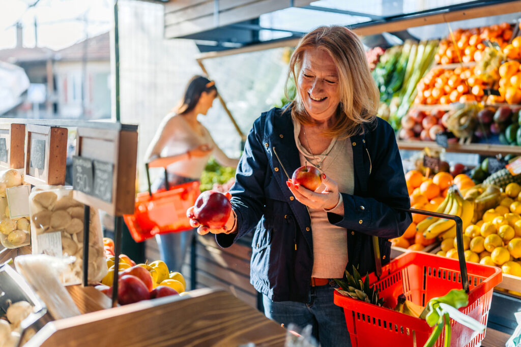 Mature woman in the produce section of a grocery store looking at apples