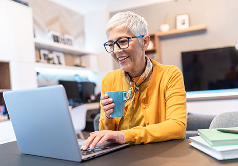 senior woman working on her laptop enjoying a cup of coffee